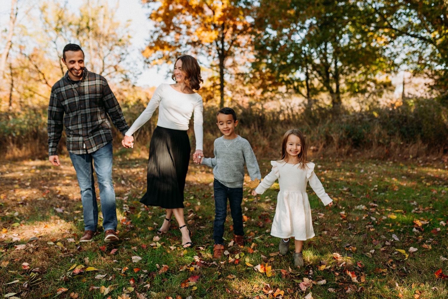 Happy family of four holding hands and walking through a colorful autumn park.