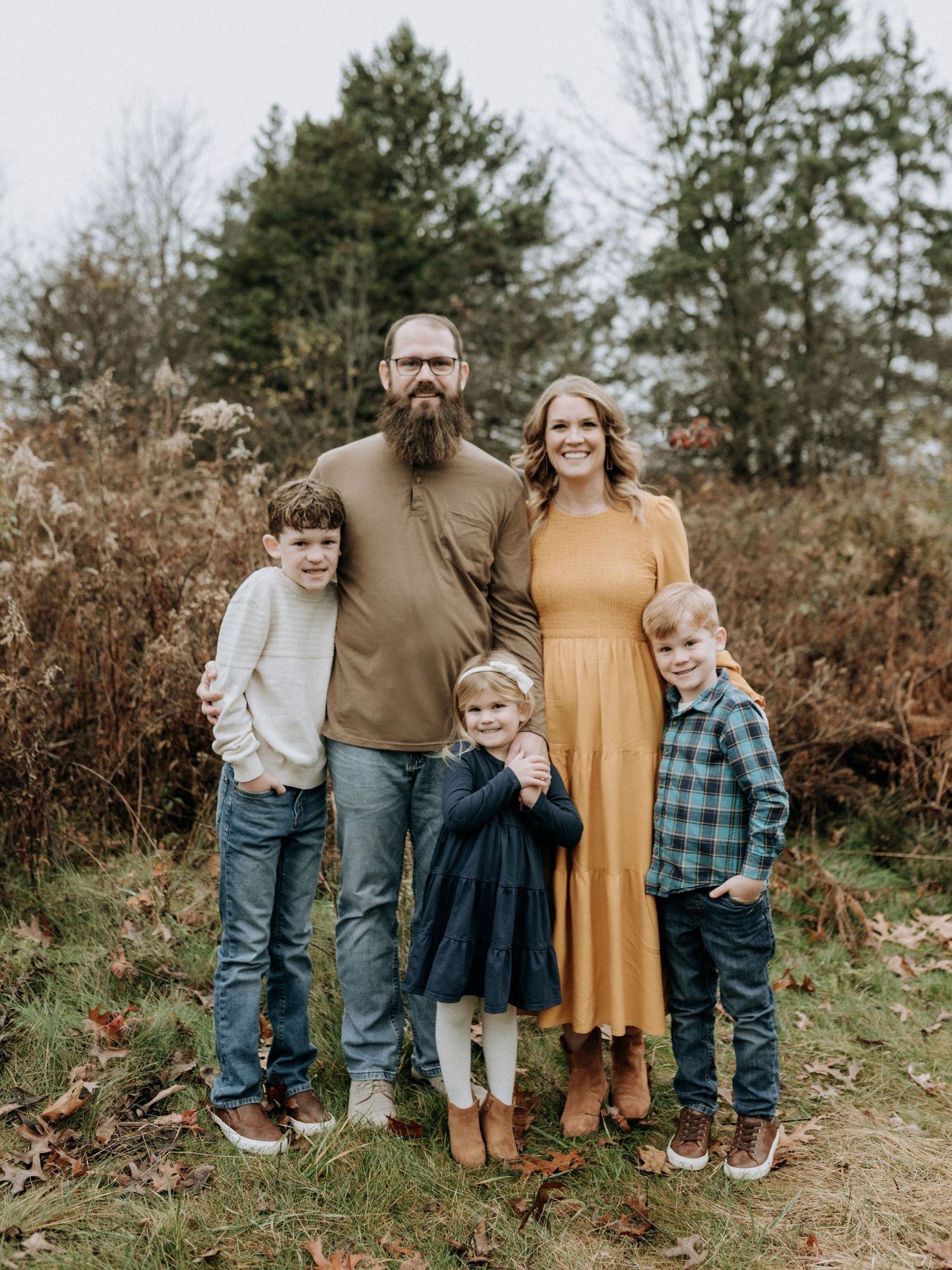 Family of five posing outdoors in fall foliage, parents with three young children in coordinated autumn outfits at Succop Nature Park in PA.