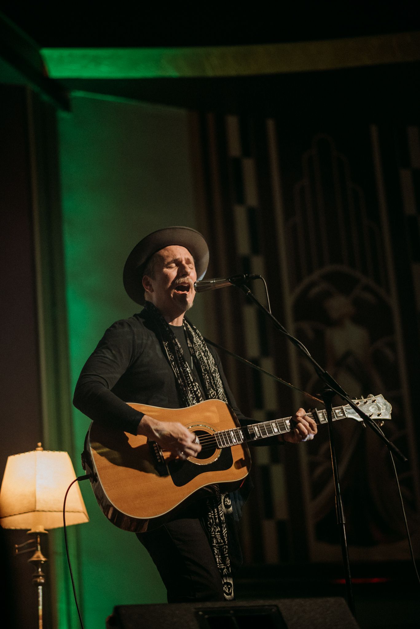 Shane Alexander, a musician performs on stage at The Penn Theater playing acoustic guitar under green stage lighting in a concert venue.