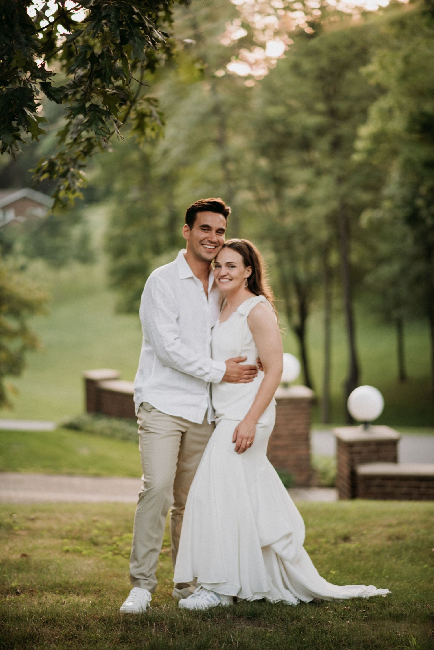Happy couple embraces and smiles together in a scenic green park during their wedding portraits.