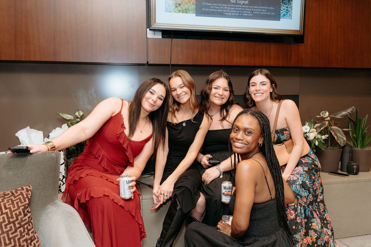 Five women posing together at a formal event, smiling for the camera in elegant dresses.