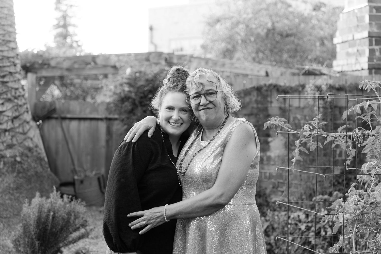 Family celebrating milestone birthday Two women smiling and embracing outdoors in a garden setting, black and white portrait photo.