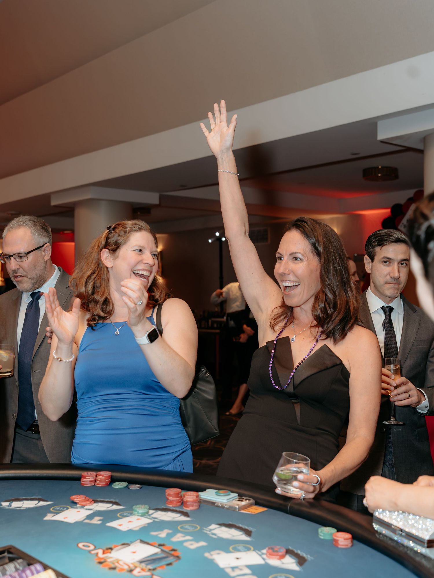 Corporate non profit event  where People celebrating and raising their hands excitedly while playing a card game at a party gathering.