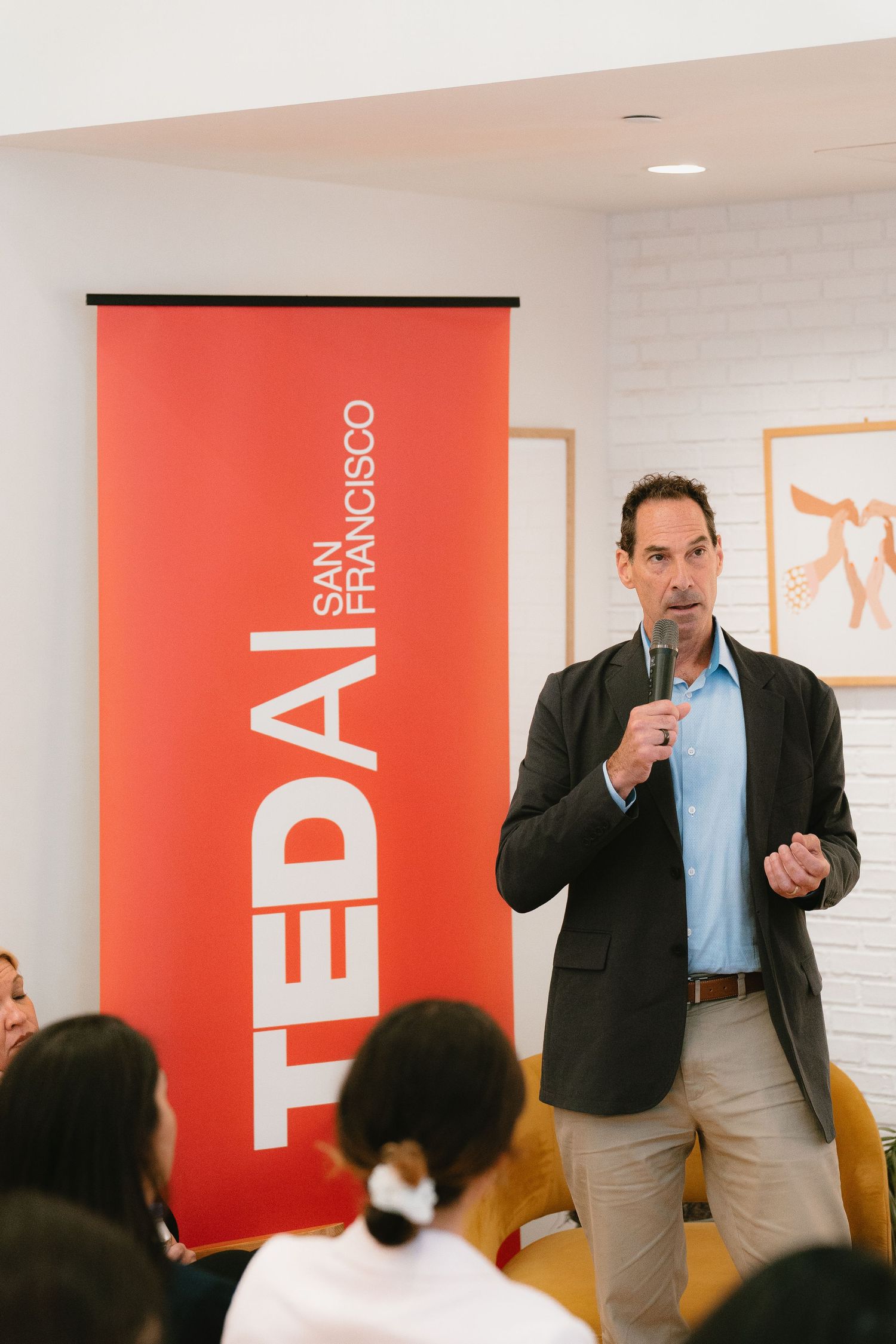 Speaker presenting at TED AI San Francisco event, holding microphone in modern white venue.