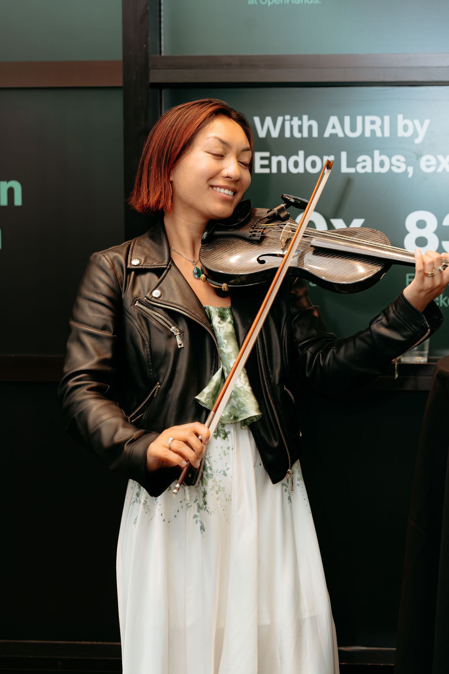 corporate event for tech company in tech industry Woman in leather jacket smiling while playing violin at Endor Labs AURI event.