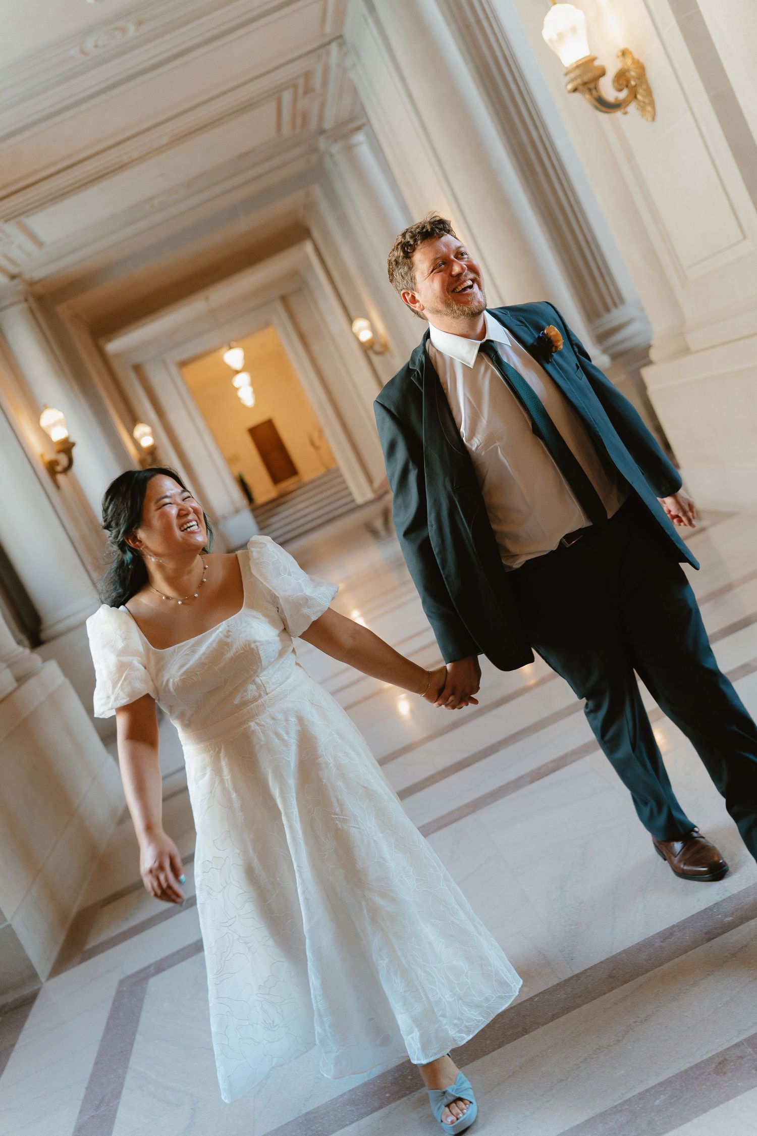 Joyful newlyweds holding hands and laughing while walking down elegant steps at San Francisco City Hall.