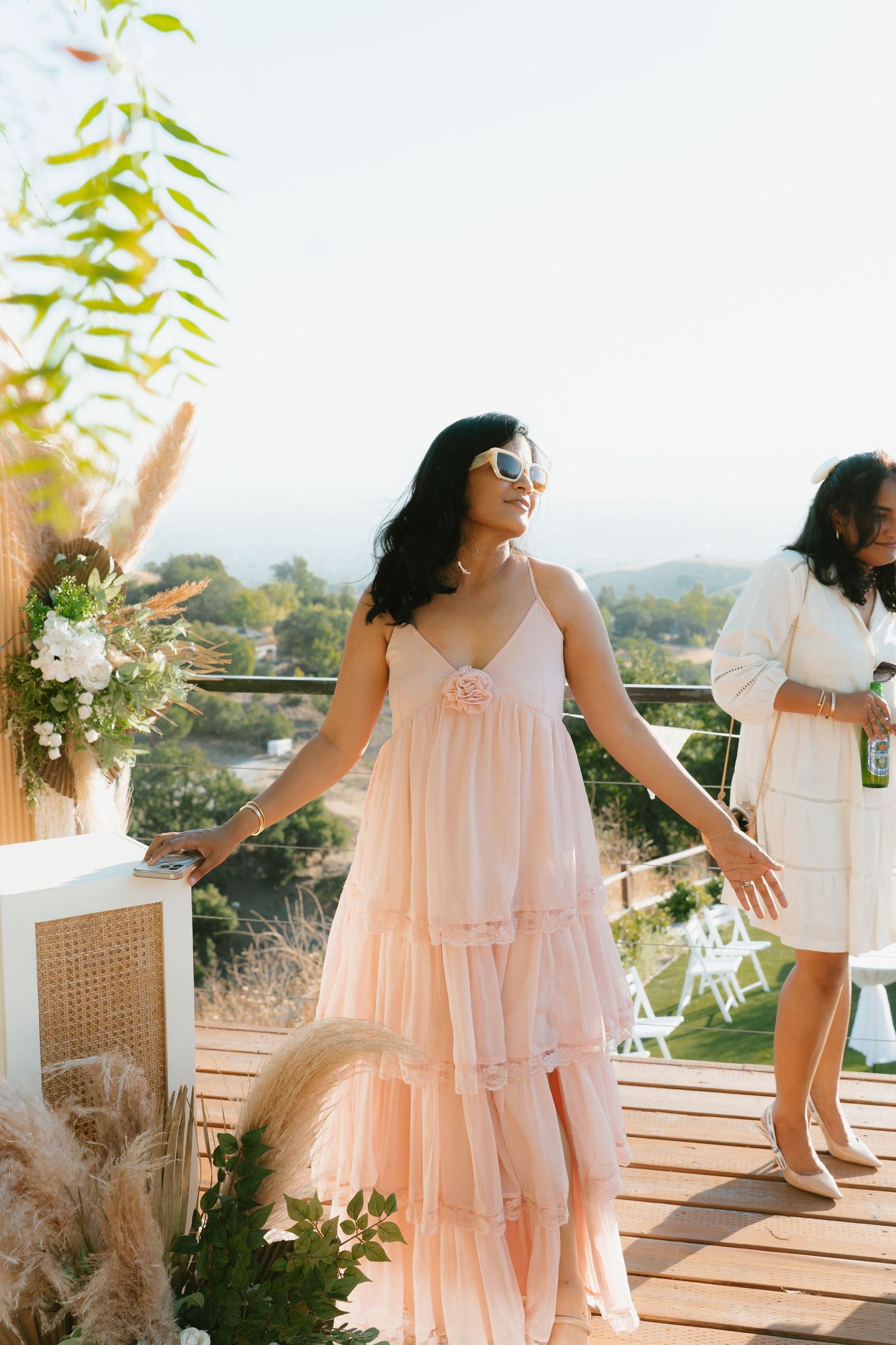 Woman in flowing pink tulle dress poses on outdoor deck at a sunny wedding venue.