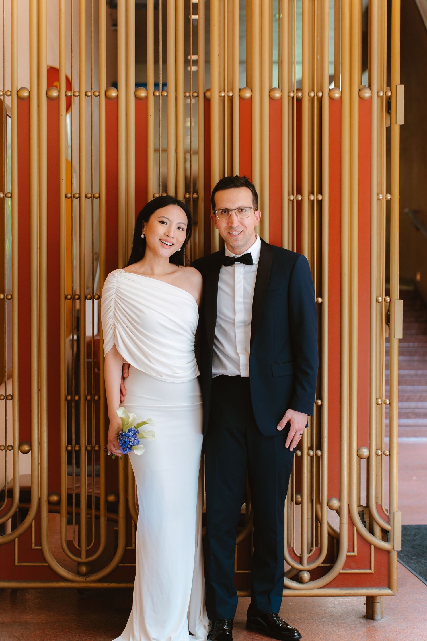 Bride in white gown and groom in black tuxedo posing together in front of gold Art Deco decor at the Marin County civic center for their civ