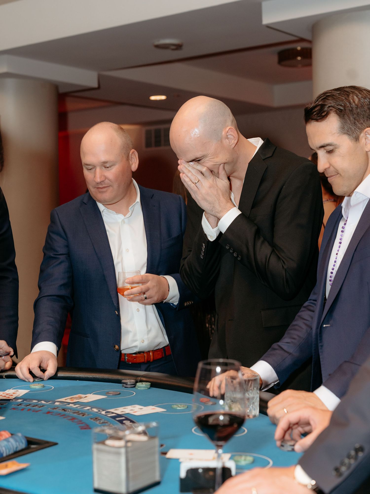 Corporate non profit event  where A group of men in suits playing casino games at a blackjack table with wine glasses.