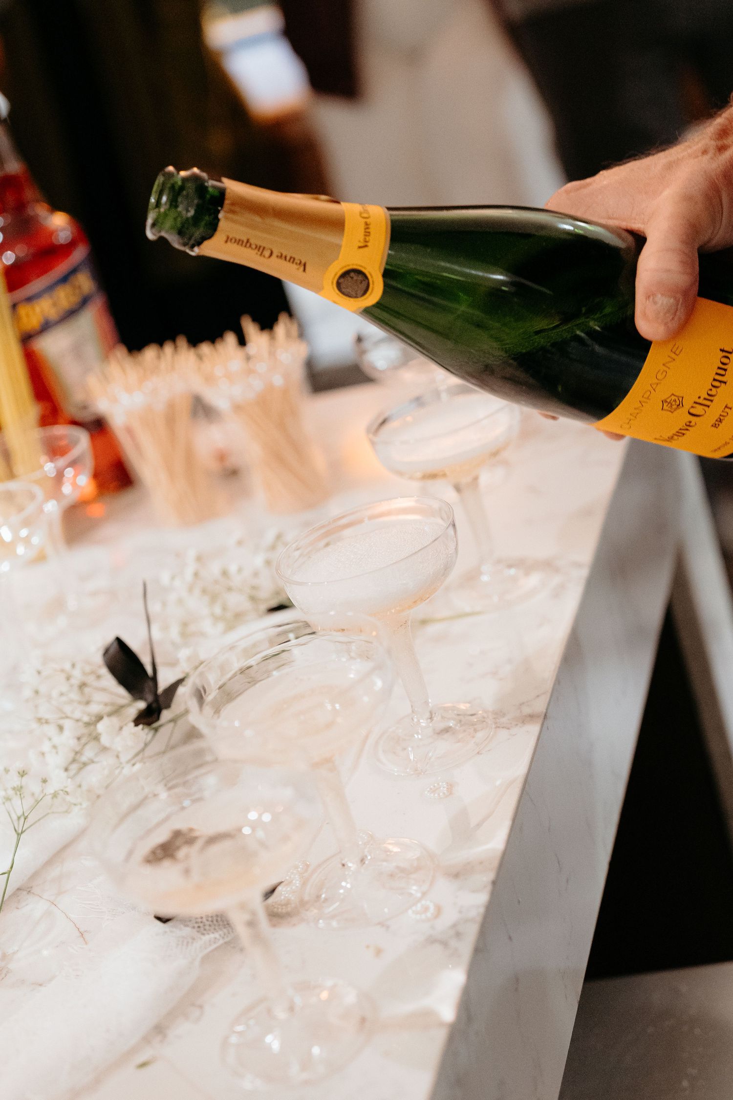 Hand pouring Veuve Clicquot champagne into elegant glasses on a marble bar at an upscale event.