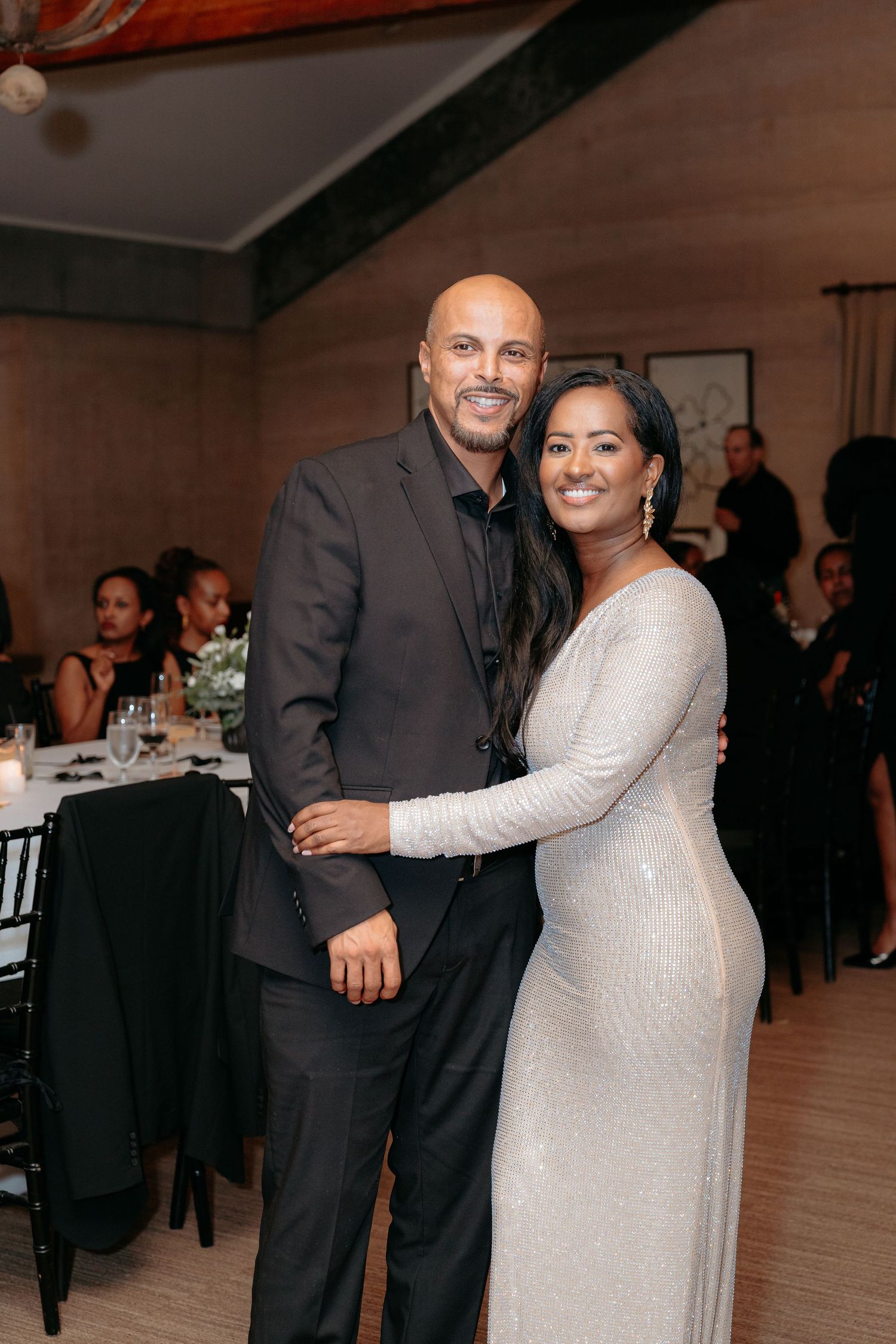 Elegant couple posing together at a formal event, man in dark suit, woman in silver sequined gown.