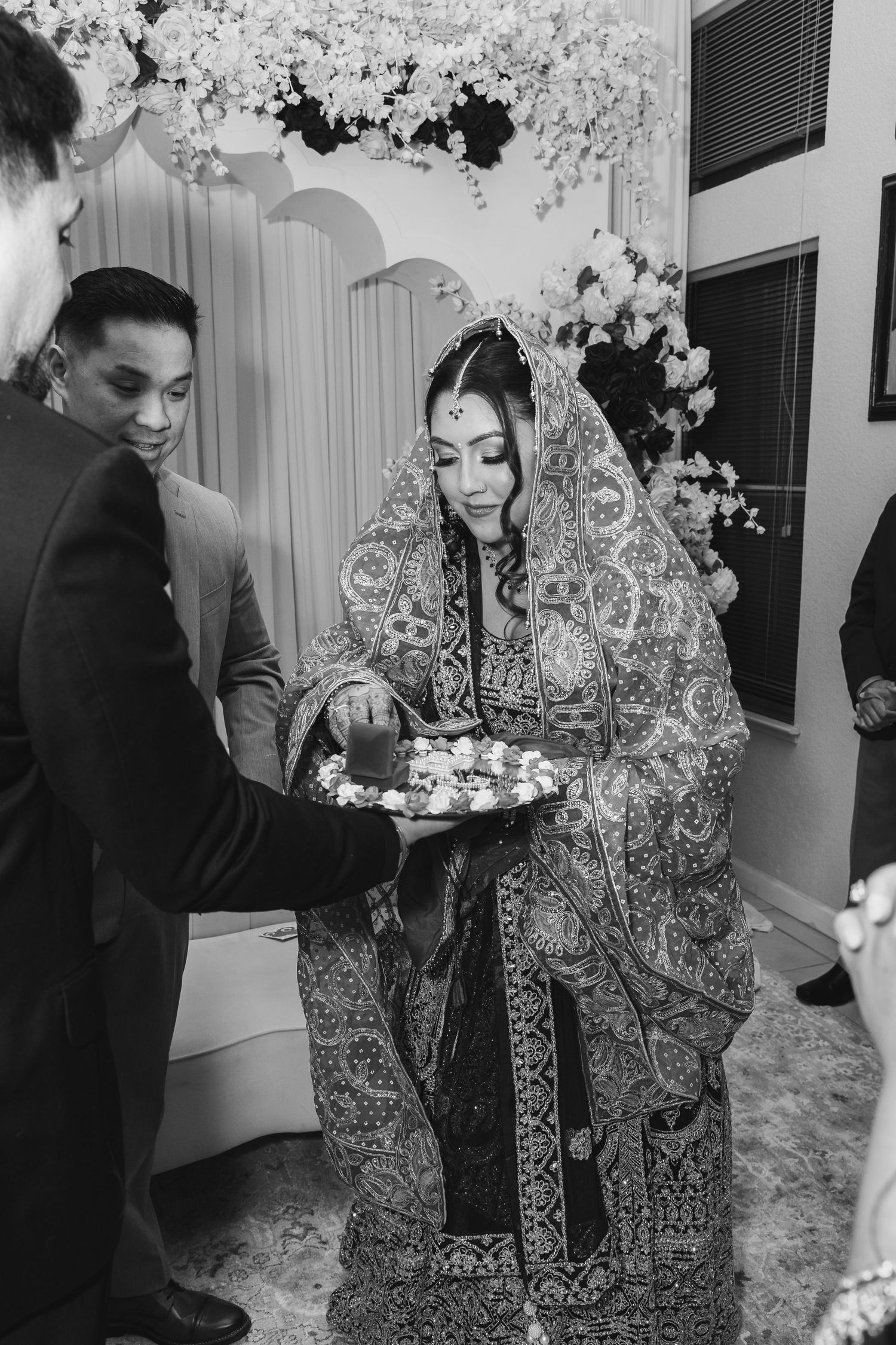 Bride in ornate dupatta holding floral plate during traditional South Asian wedding ceremony.