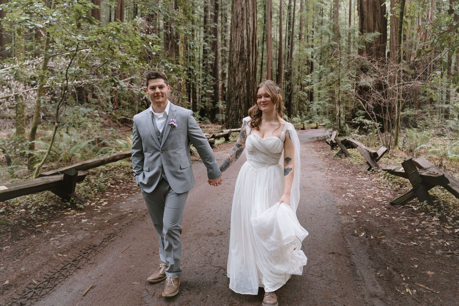 Bride and groom holding hands walking through a redwood forest on their wedding day.