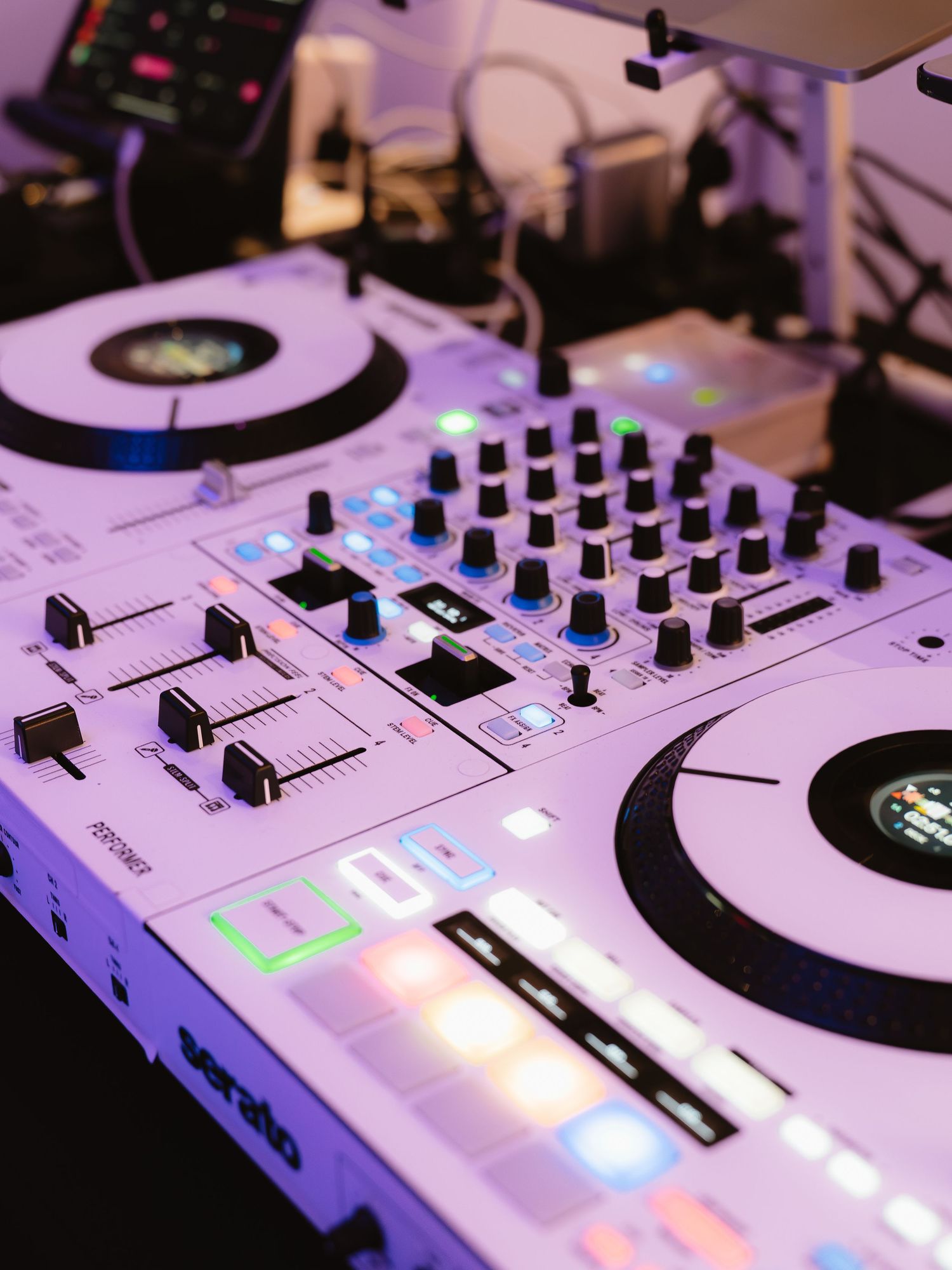 A professional DJ controller with illuminated colorful pads, faders, and jog wheels glowing in purple light on a mixing table.