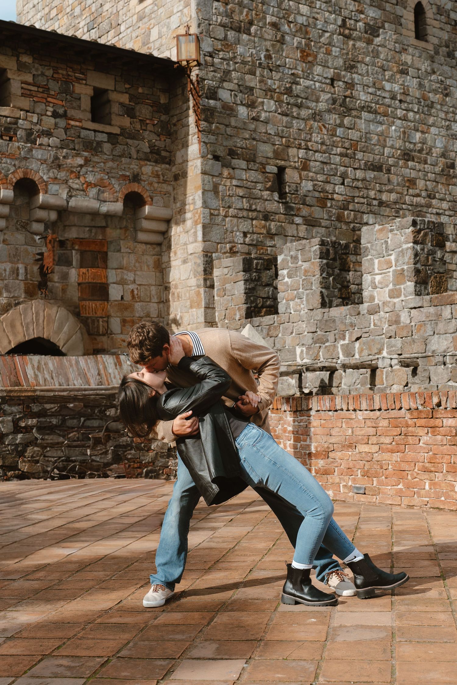 A person in jeans and leather jacket performs a dynamic breakdance move sequence on stone floor tiles.