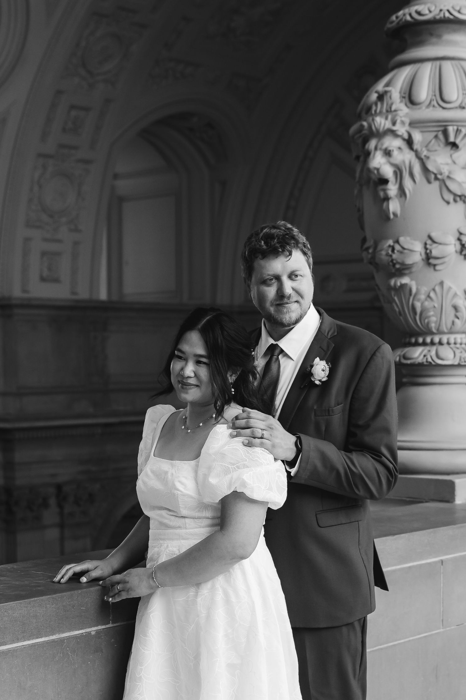 Black and white wedding portrait of a couple posing elegantly in an ornate architectural setting with decorative columns.