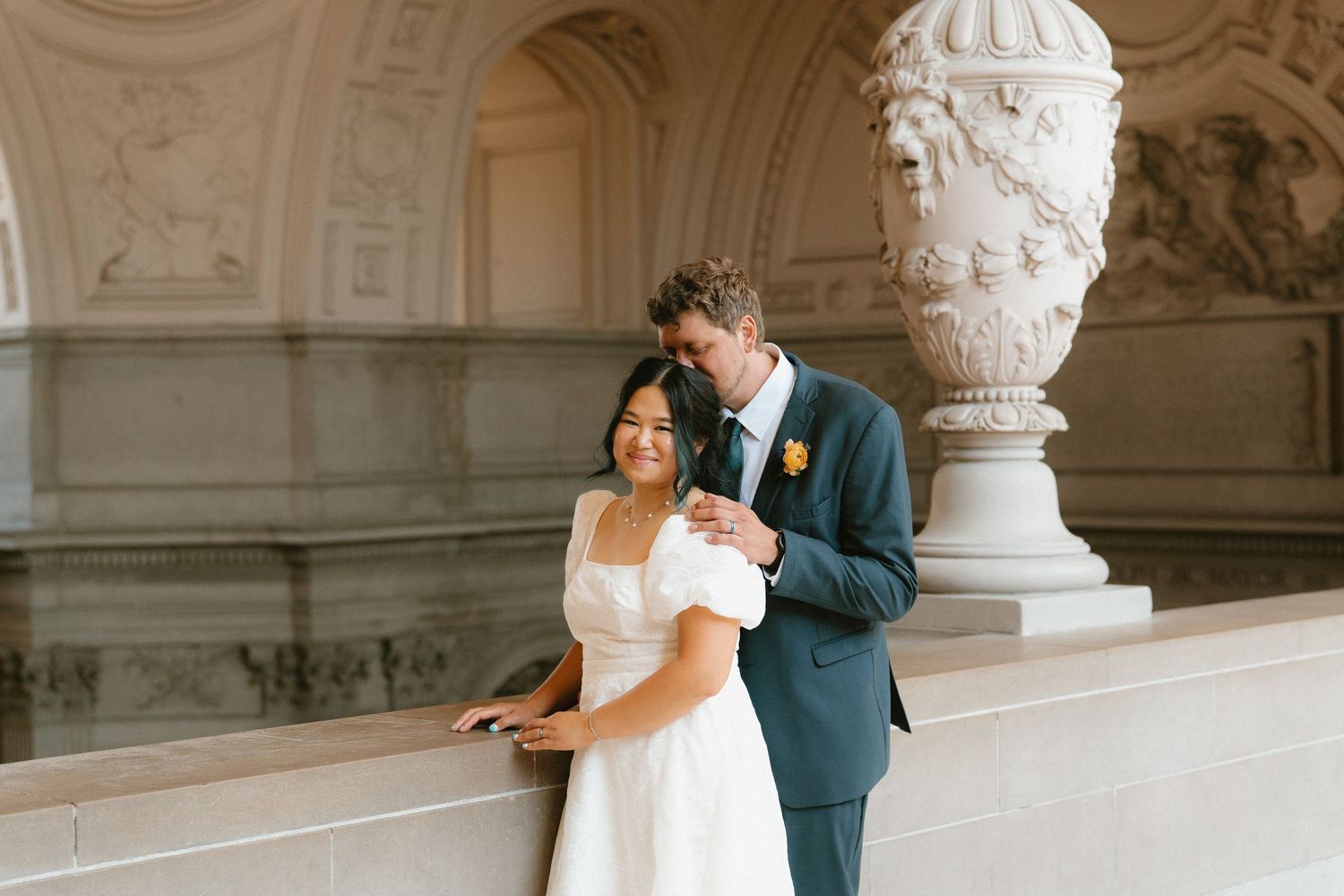 Bride and groom share a romantic moment at San Francisco City Hall, with elegant marble columns and ornate architecture.