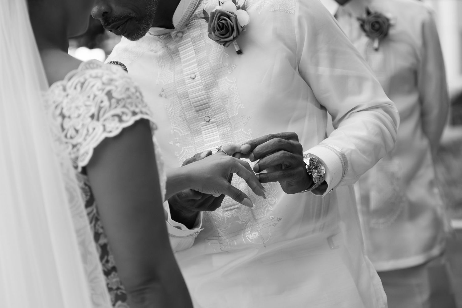 Black and white photo of bride and groom exchanging wedding rings during ceremony.