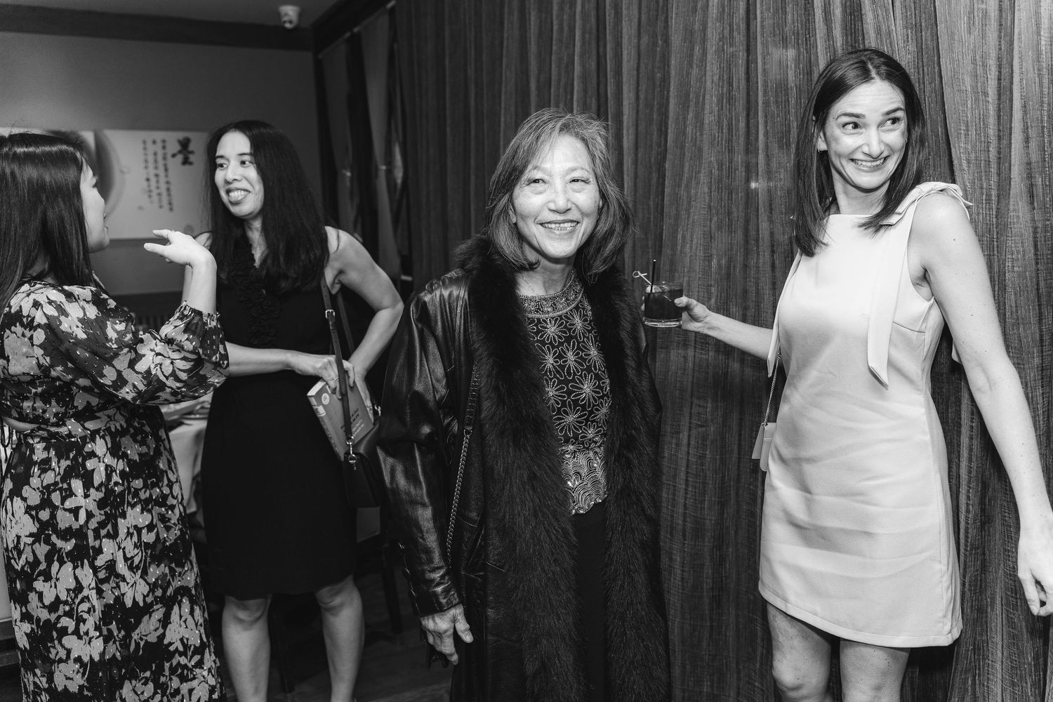 Black and white photo of three elegant women smiling and socializing at a formal indoor event.
