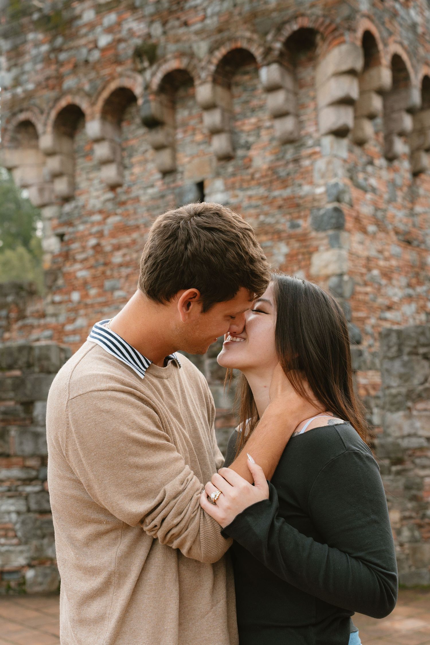 Romantic couple almost kissing in front of an ancient brick wall architecture.