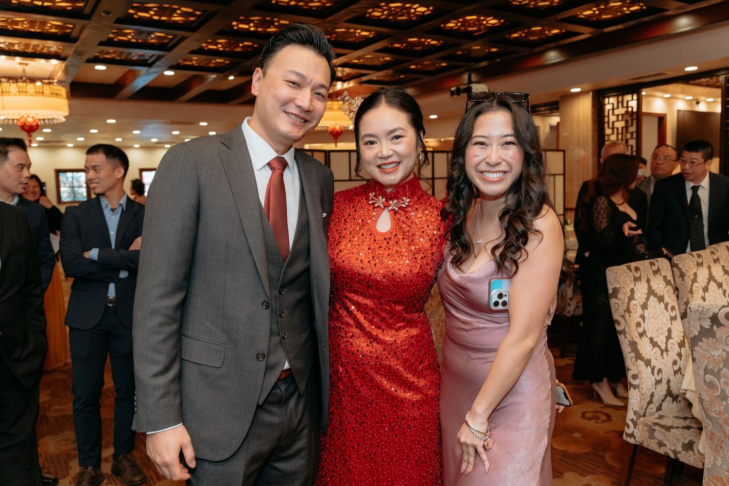 Three elegantly dressed guests smile together at a formal Asian banquet celebration.