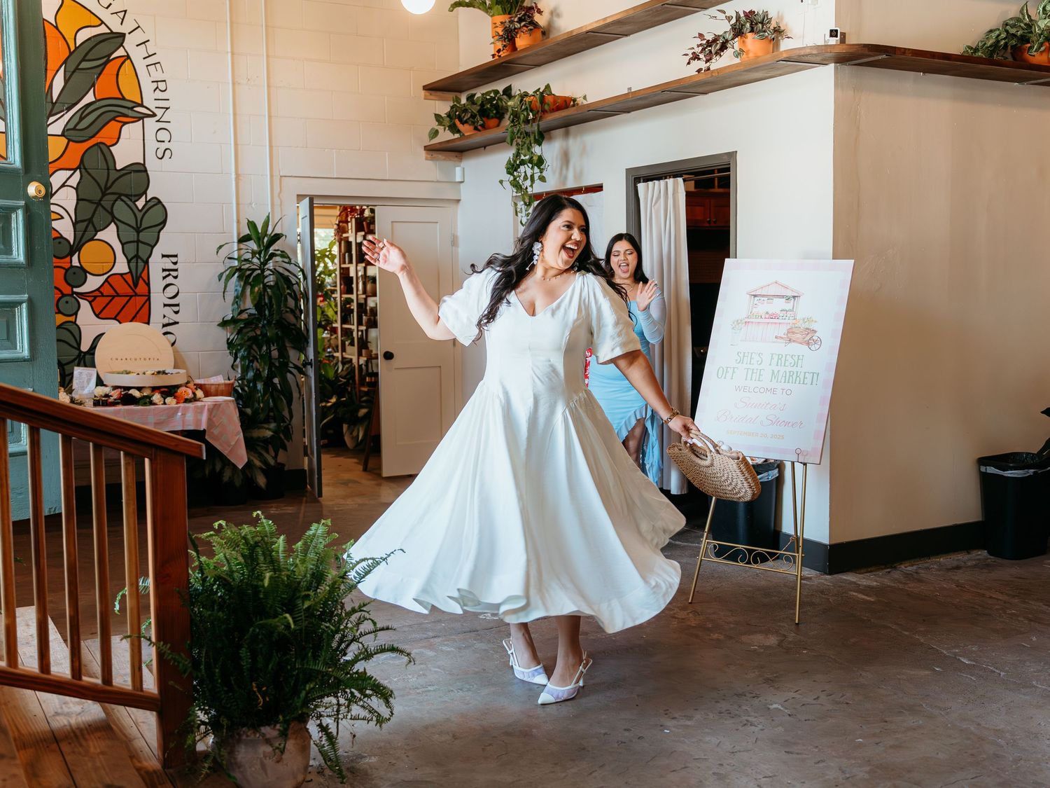 Bride in white midi dress twirling joyfully inside a decorated venue with plants and stained glass.