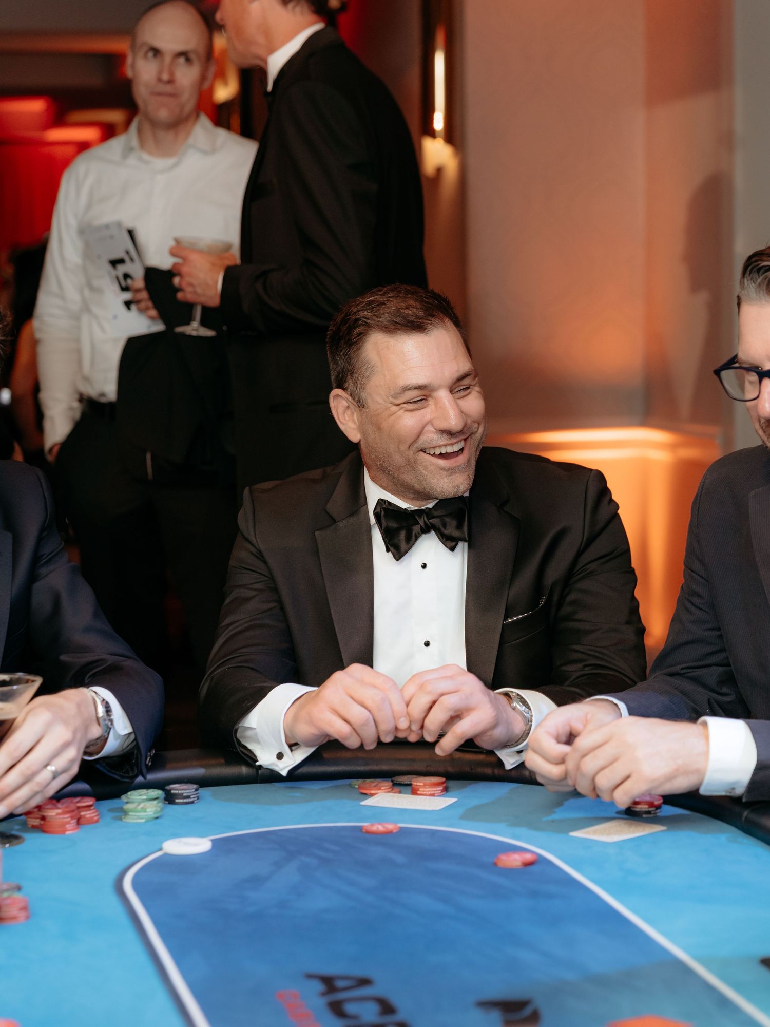Corporate non profit event  where  People gathered around a blue casino table playing cards and laughing during an elegant event.