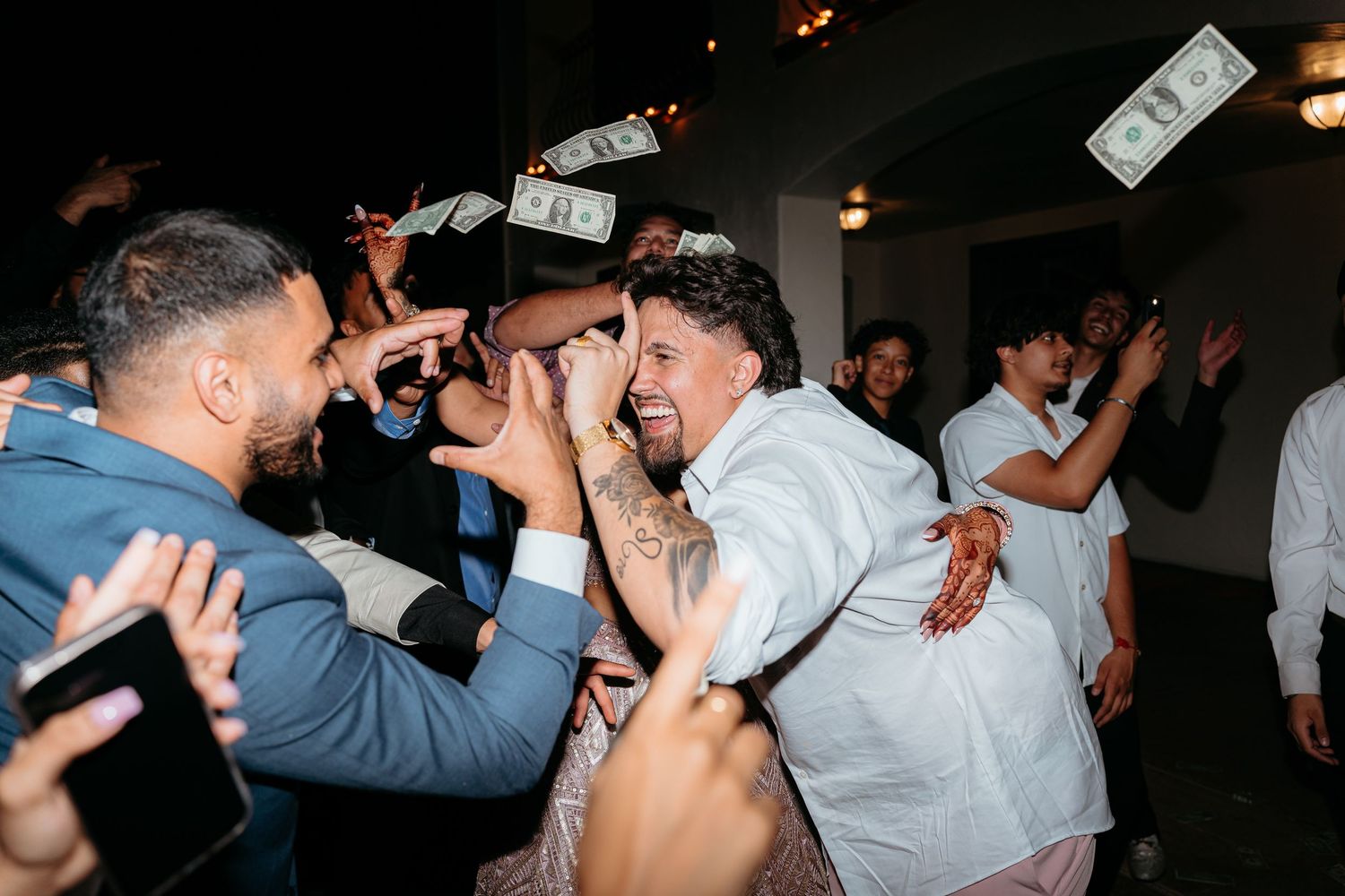 Joyful wedding reception dance floor celebration with guests throwing dollar bills at the happy couple.