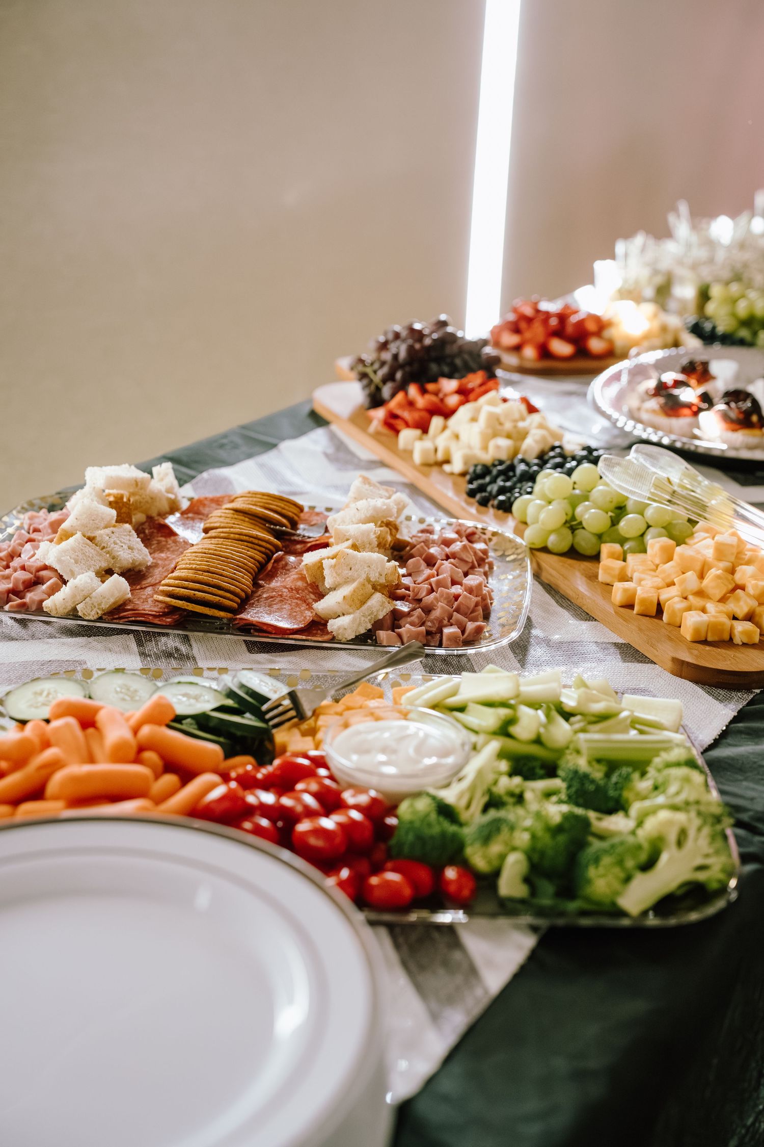 A buffet table with charcuterie, crackers, fresh vegetables, dips, fruits, and cheese arranged on platters for an event.
