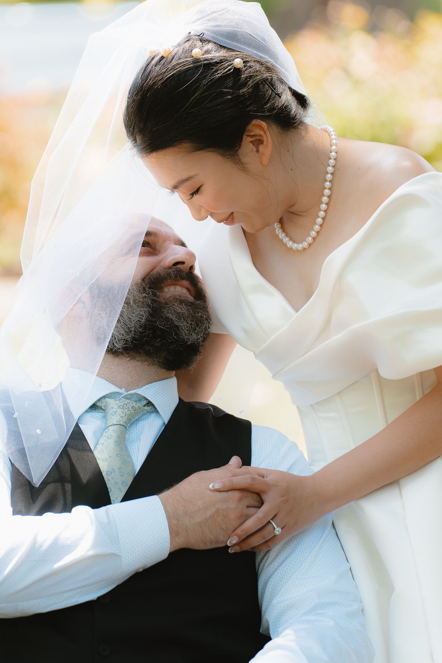 Bride and groom share an intimate moment under a veil, bride wearing pearl necklace and white dress.
