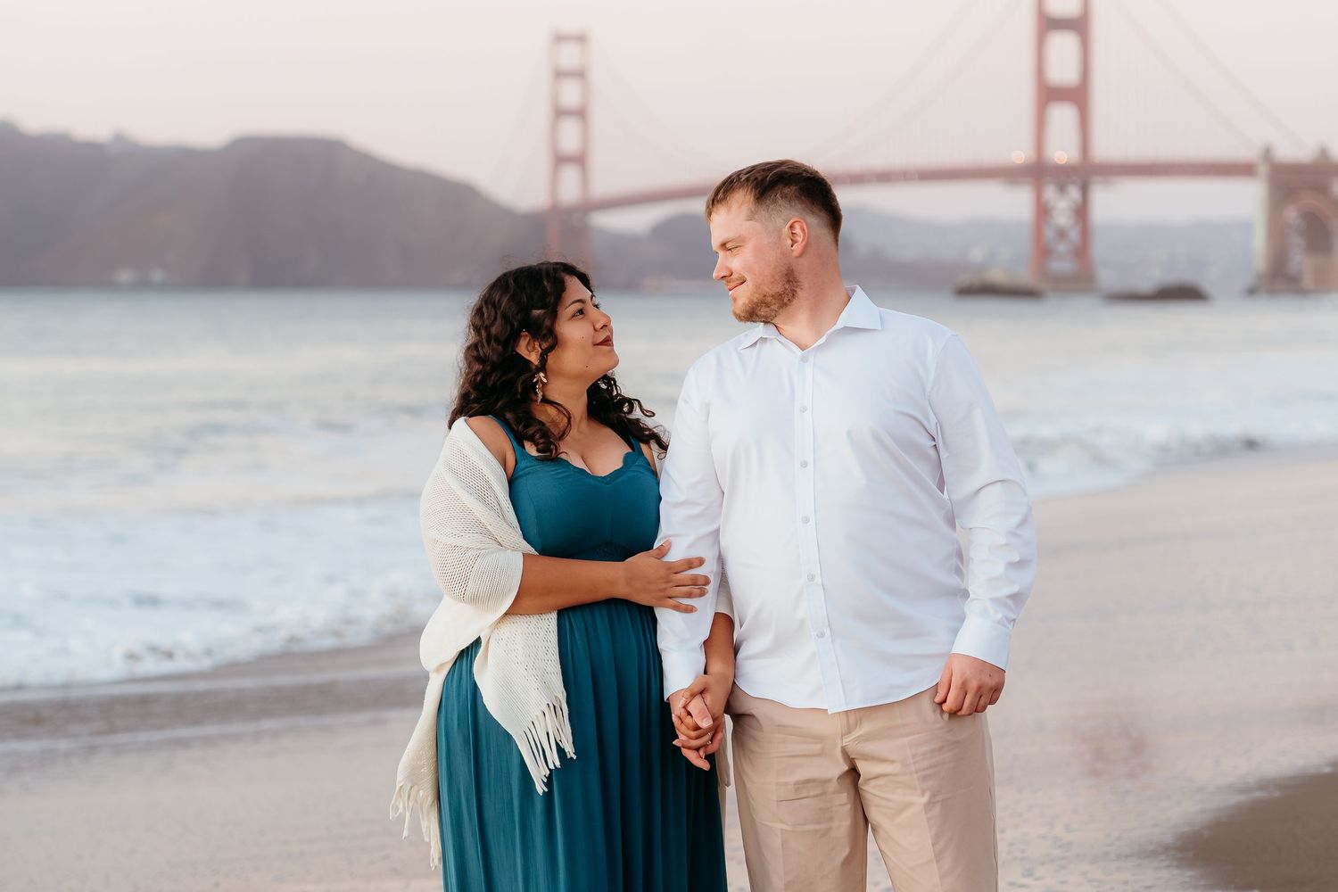 Couple holding hands on Baker Beach with Golden Gate Bridge backdrop in San Francisco.