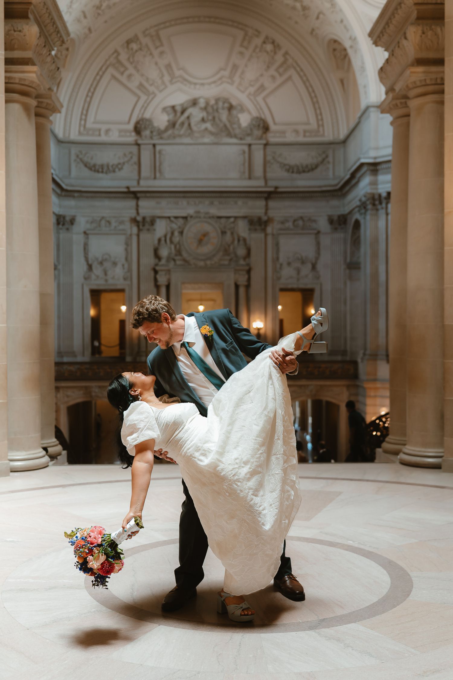 Bride and groom share a romantic dip kiss inside San Francisco City Hall's grand rotunda during their wedding ceremony.