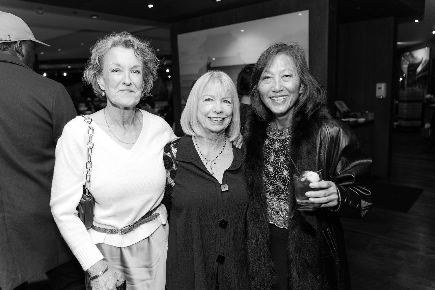 Major Milestone birthday where Three women smiling and posing together at an indoor social event in a black and white photo.