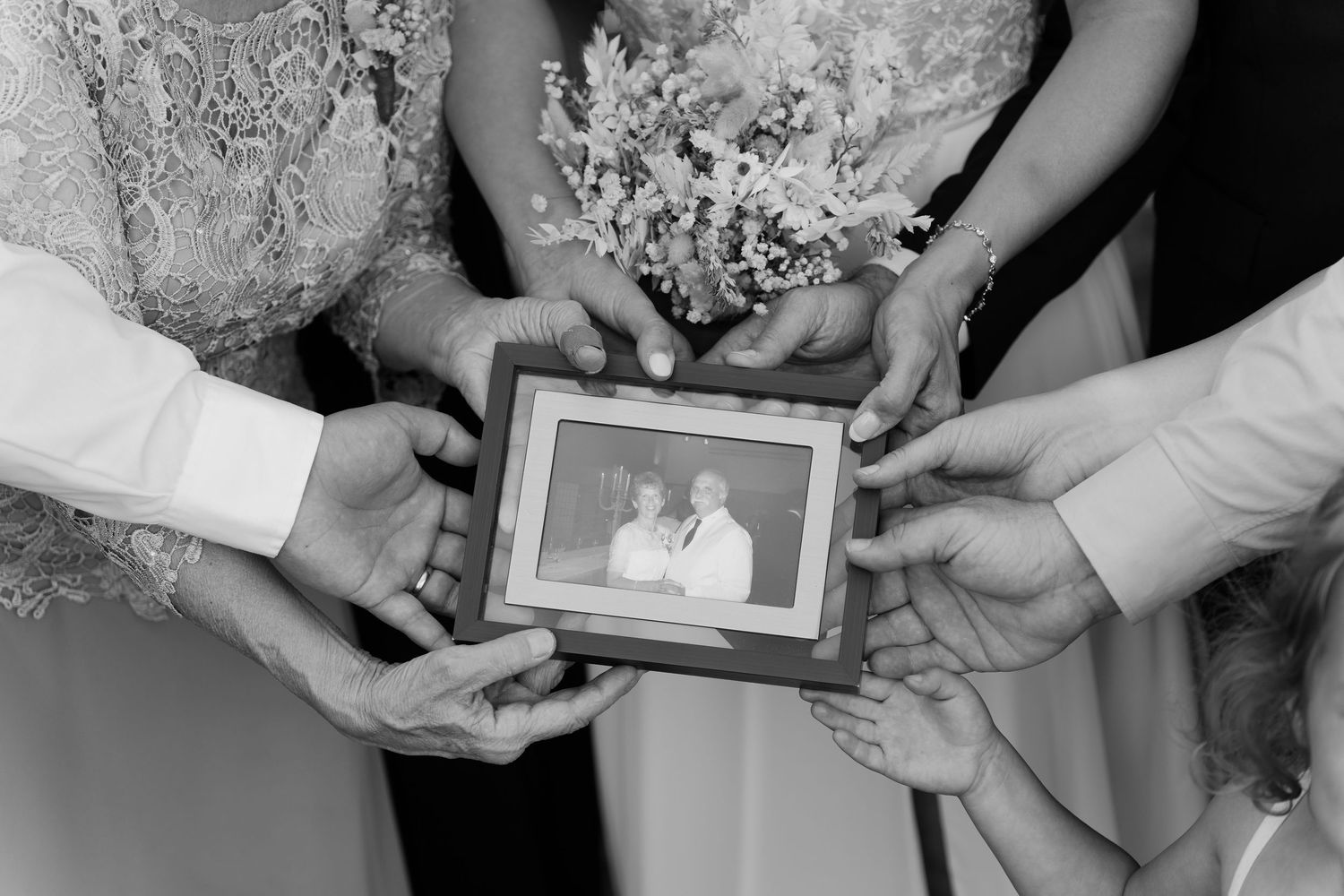 intimate wedding ceremony in Black and white photo of hands holding a framed portrait at a wedding ceremony, honoring loved ones.