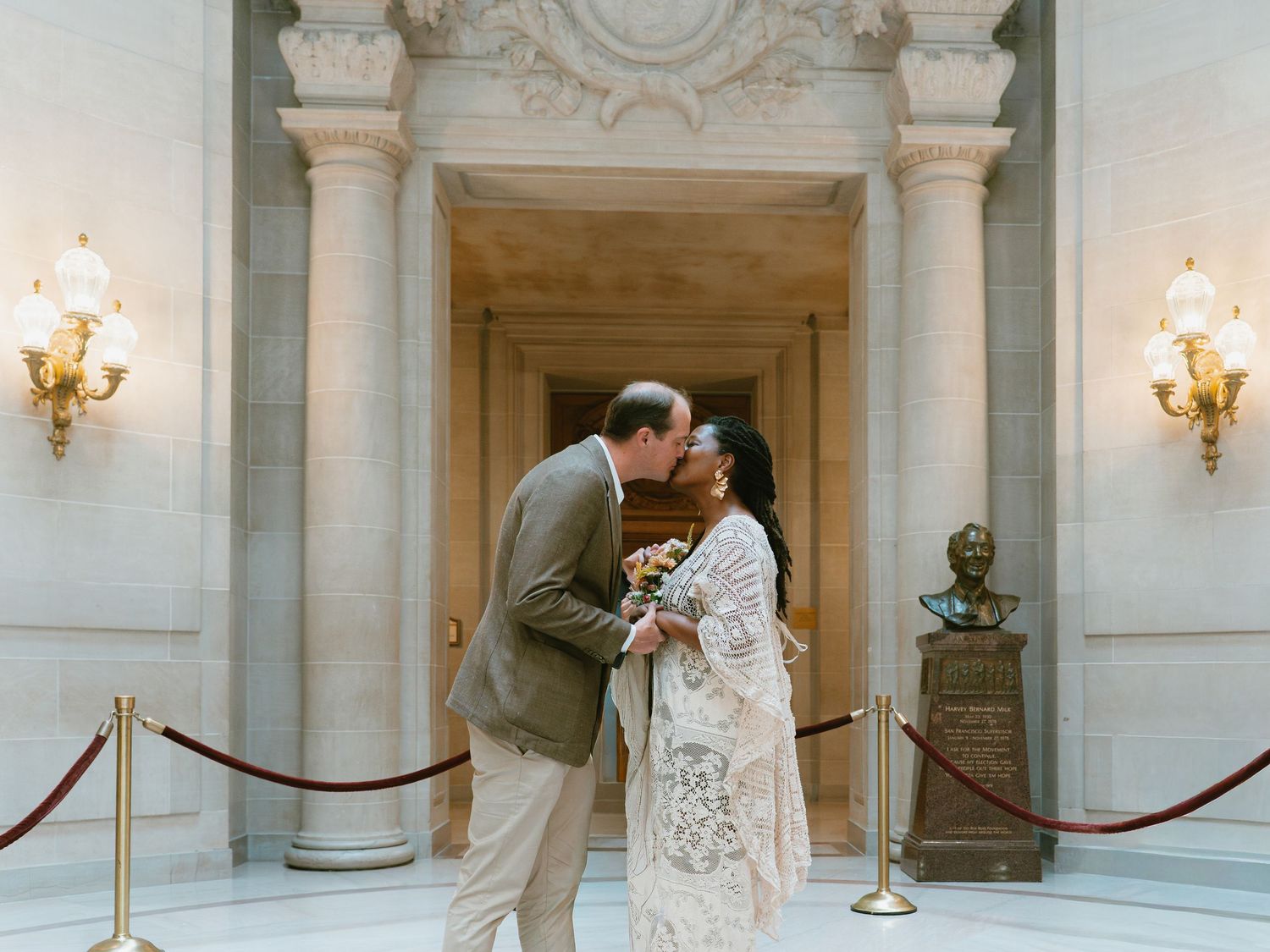 Couple sharing a first kiss at San Francisco City Hall wedding ceremony, bride in lace gown, groom in tan suit.
