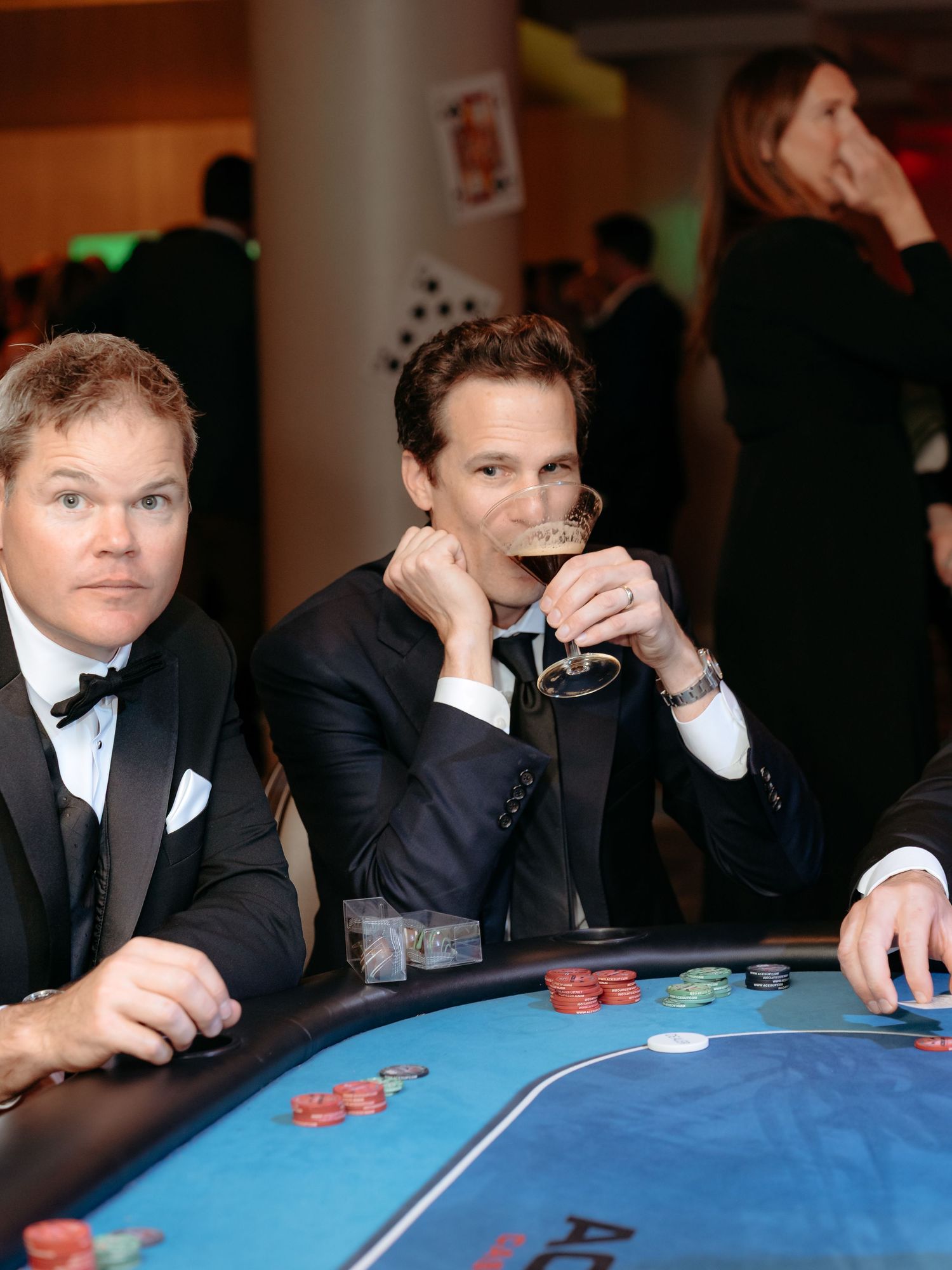 Corporate non profit event  where Well-dressed guests in suits gather around a blue casino gaming table at an event.