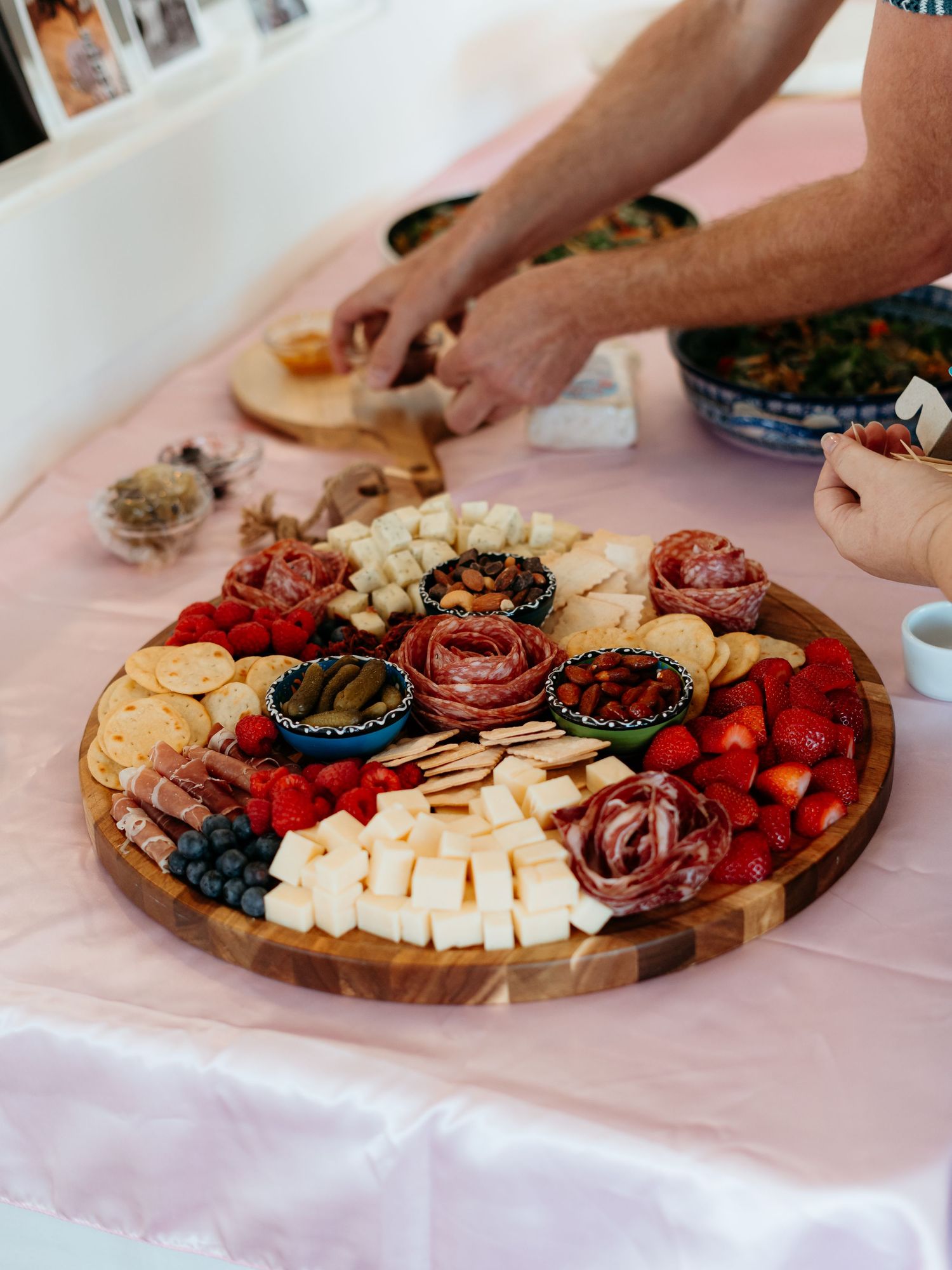 Elegant charcuterie board with cheeses, meats, fruits, and crackers on a pink tablecloth.
