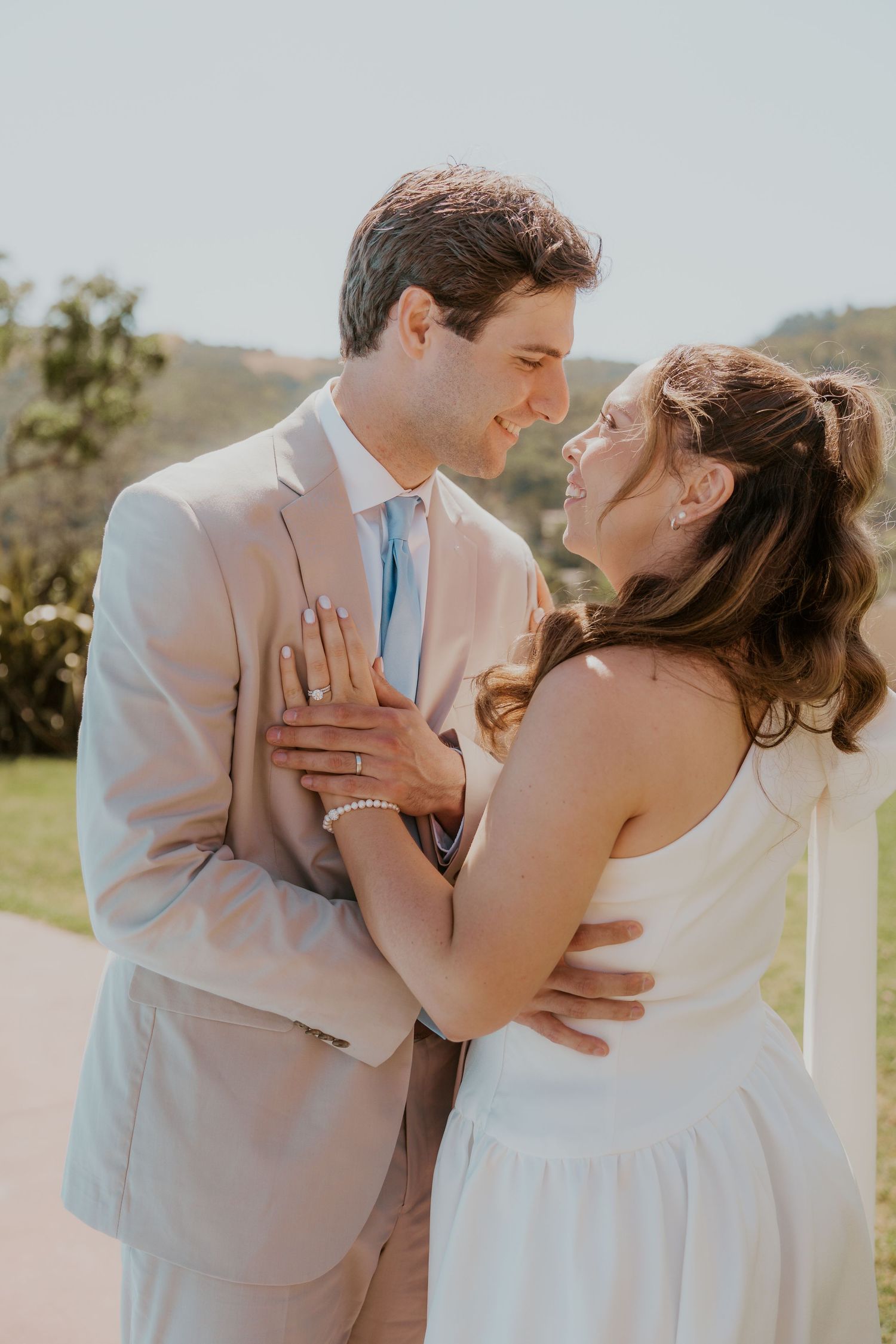 Civil ceremony at the Marin Civic Center Bride and groom share a romantic moment outdoors, dressed in white gown and tan suit with blue tie.
