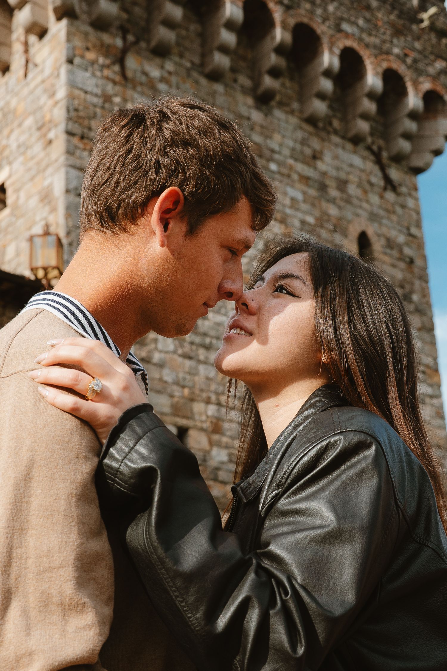 A romantic couple embraces against a rustic brick wall backdrop in warm lighting in Napa Valley winery