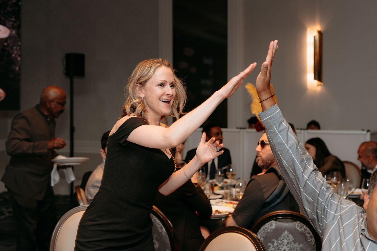 People dancing and celebrating at a lively party in a modern indoor venue with pendant lighting.