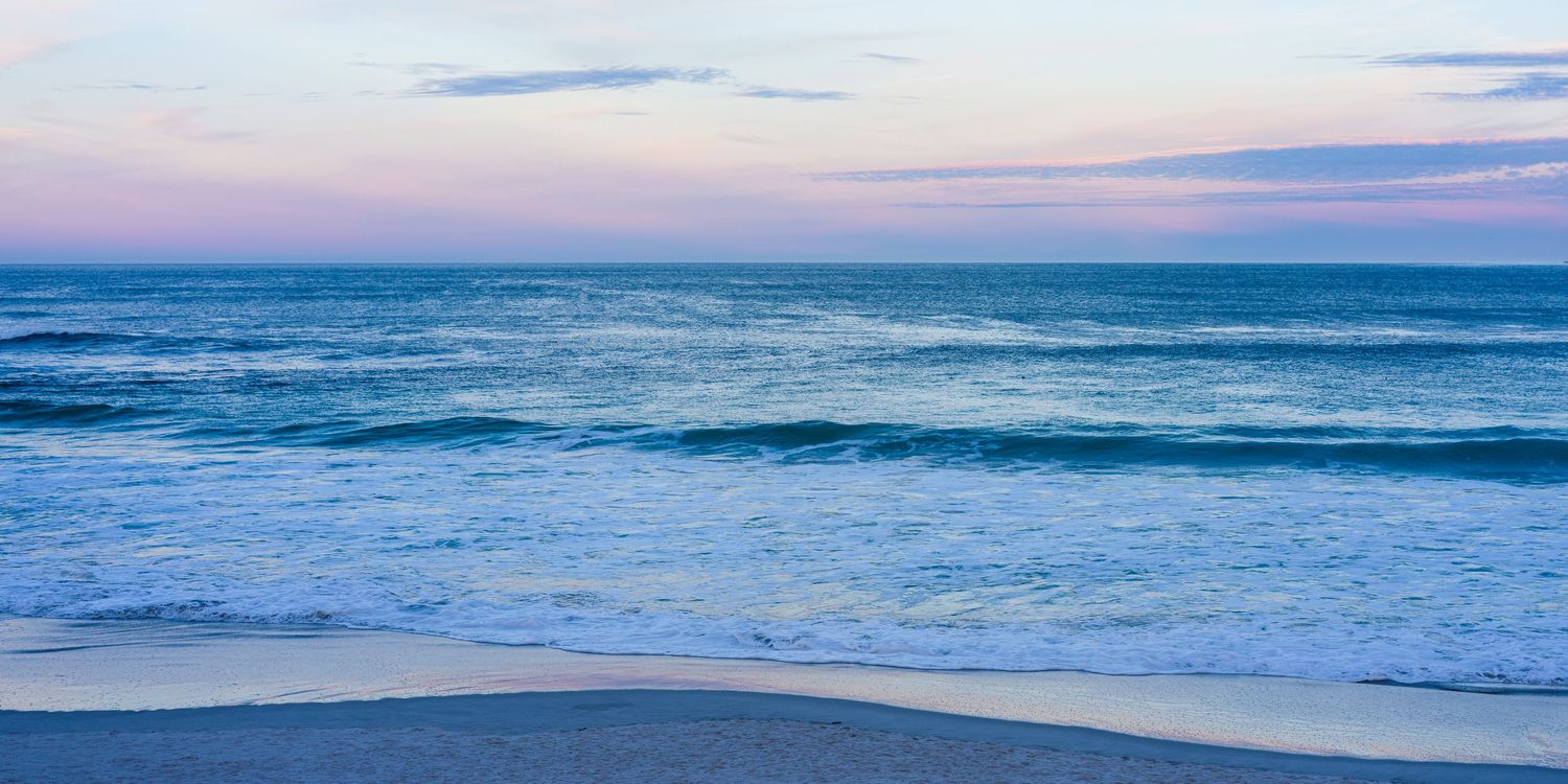 Peaceful ocean waves washing onto sandy Carmel Beach at dawn with soft blue and pink sky tones.