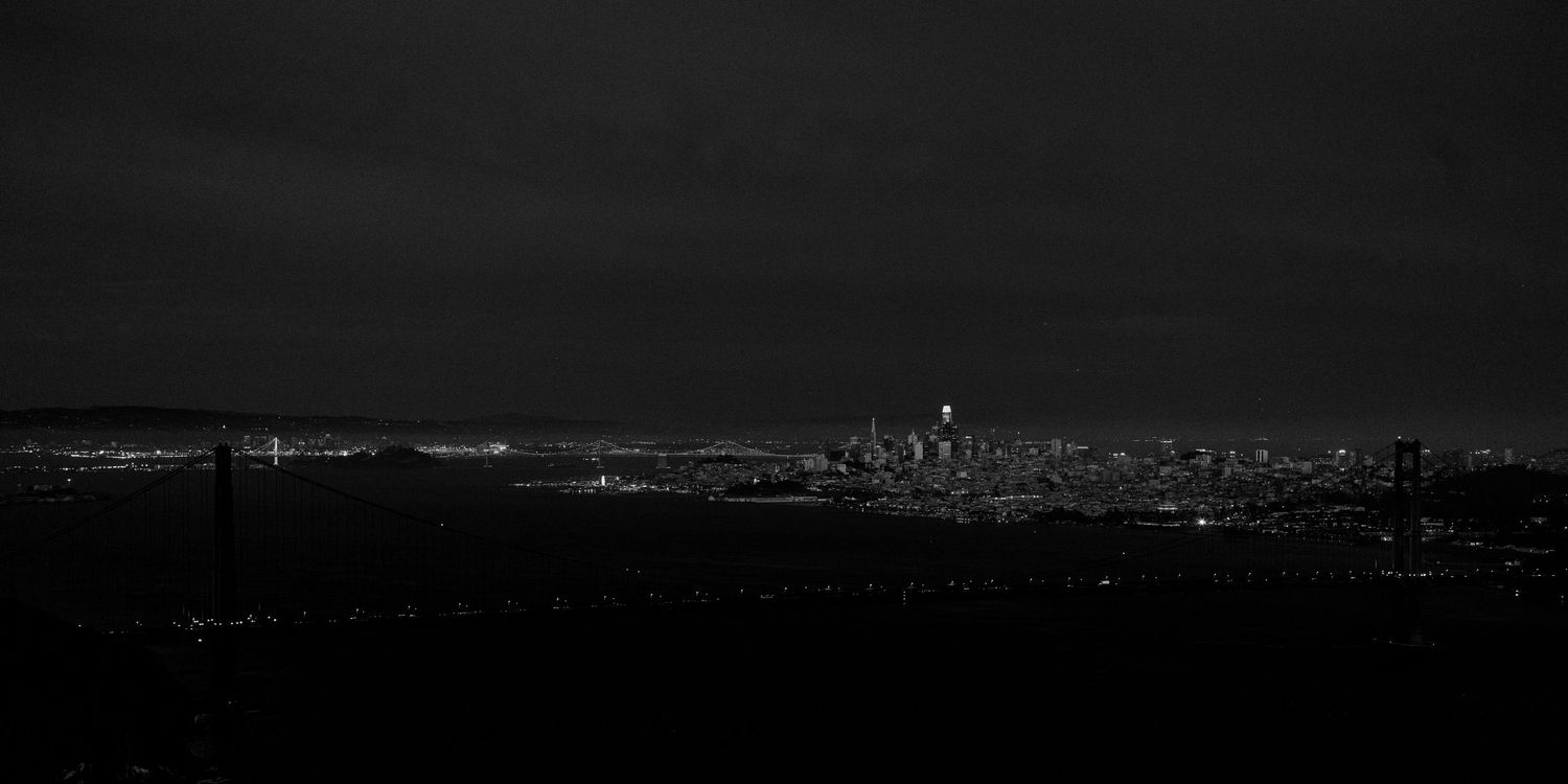Black and white panoramic night cityscape of San Francisco skyline with Golden Gate Bridge lights glowing in the dark.