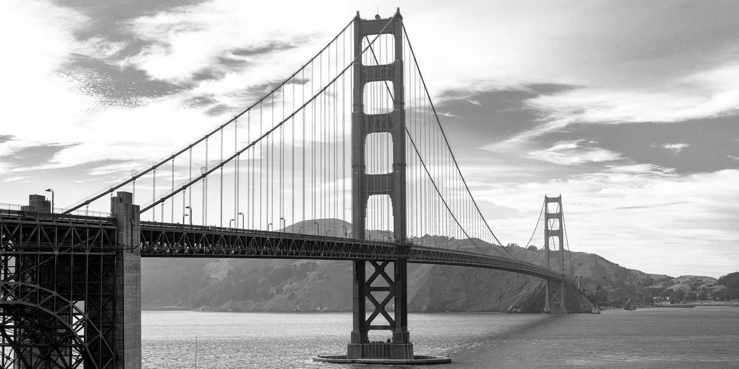 Black and white photo of the iconic Golden Gate Bridge spanning San Francisco Bay with hills in the background.