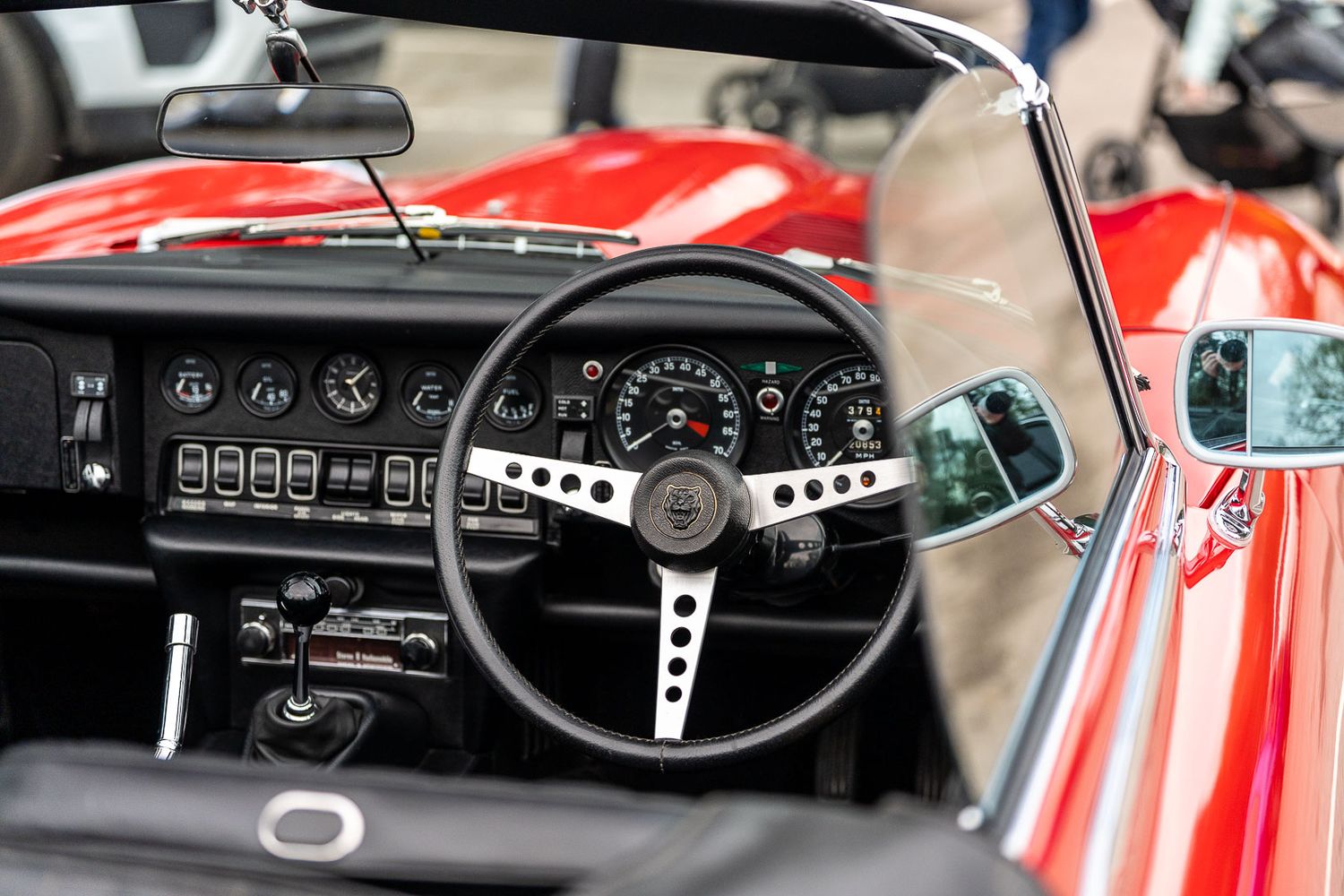 Classic red Jaguar E-Type convertible interior with vintage steering wheel and dashboard gauges.