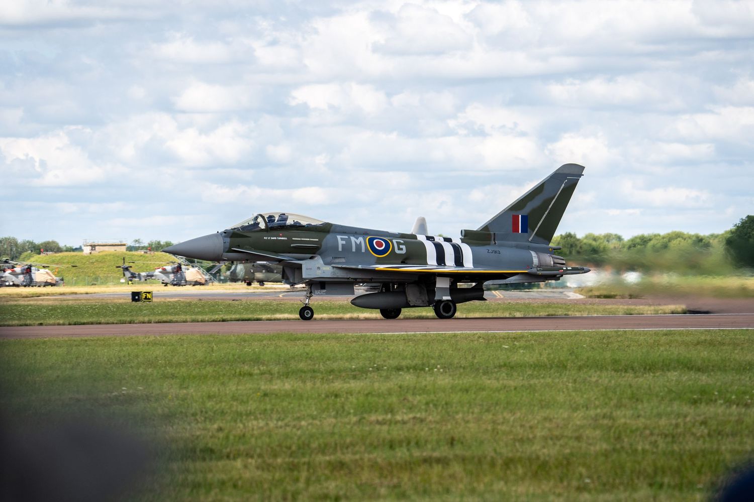RAF Eurofighter Typhoon jet in historic D-Day markings taxiing on a grass airfield.