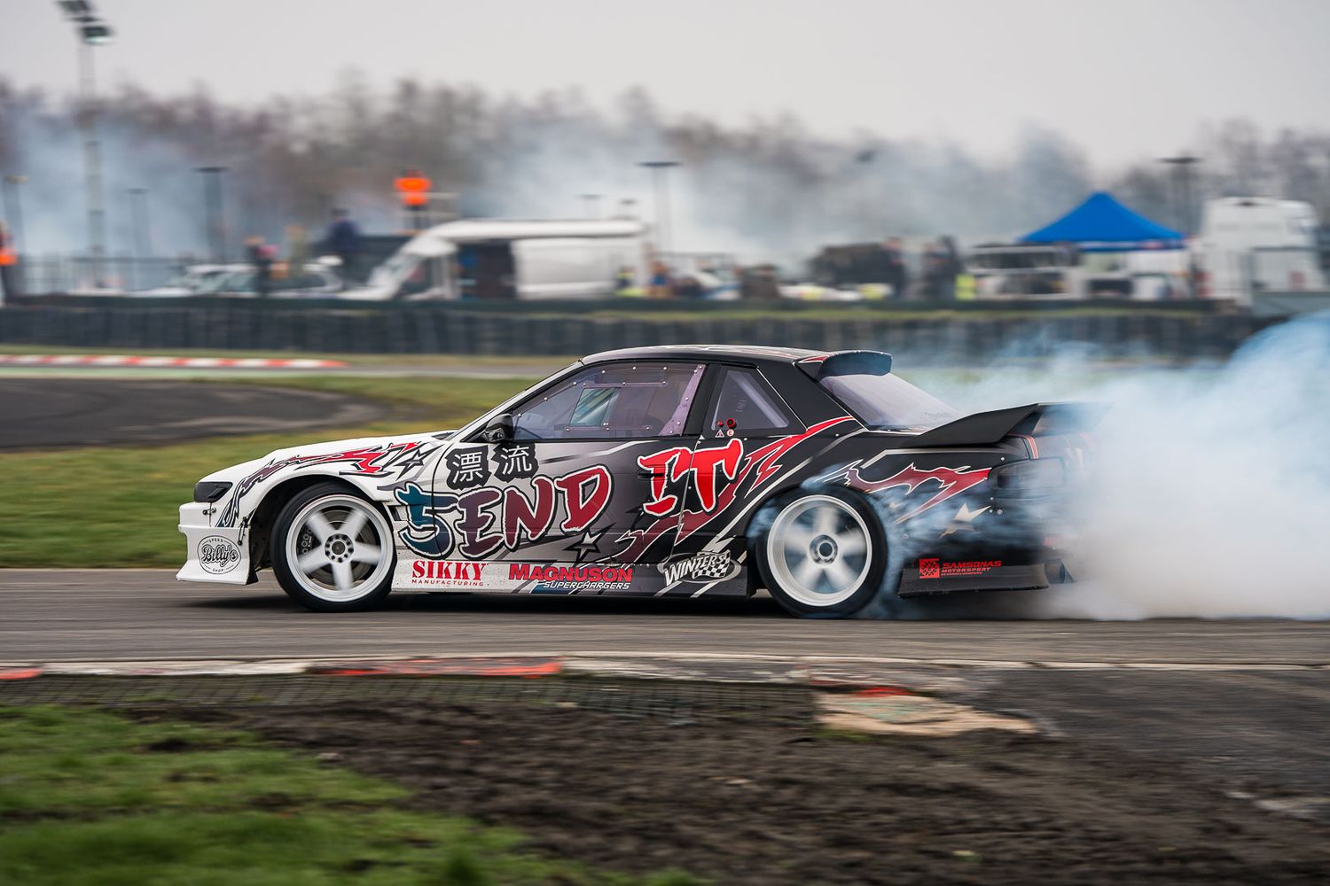 Drift car with End It livery producing heavy tire smoke on a racing circuit.