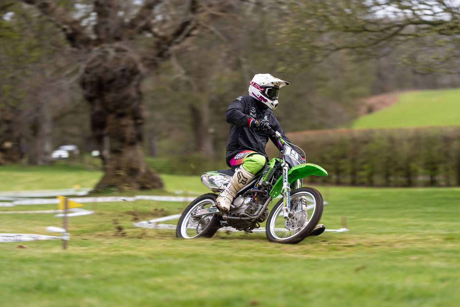 Young rider on a green Kawasaki dirt bike racing across a muddy grass field.