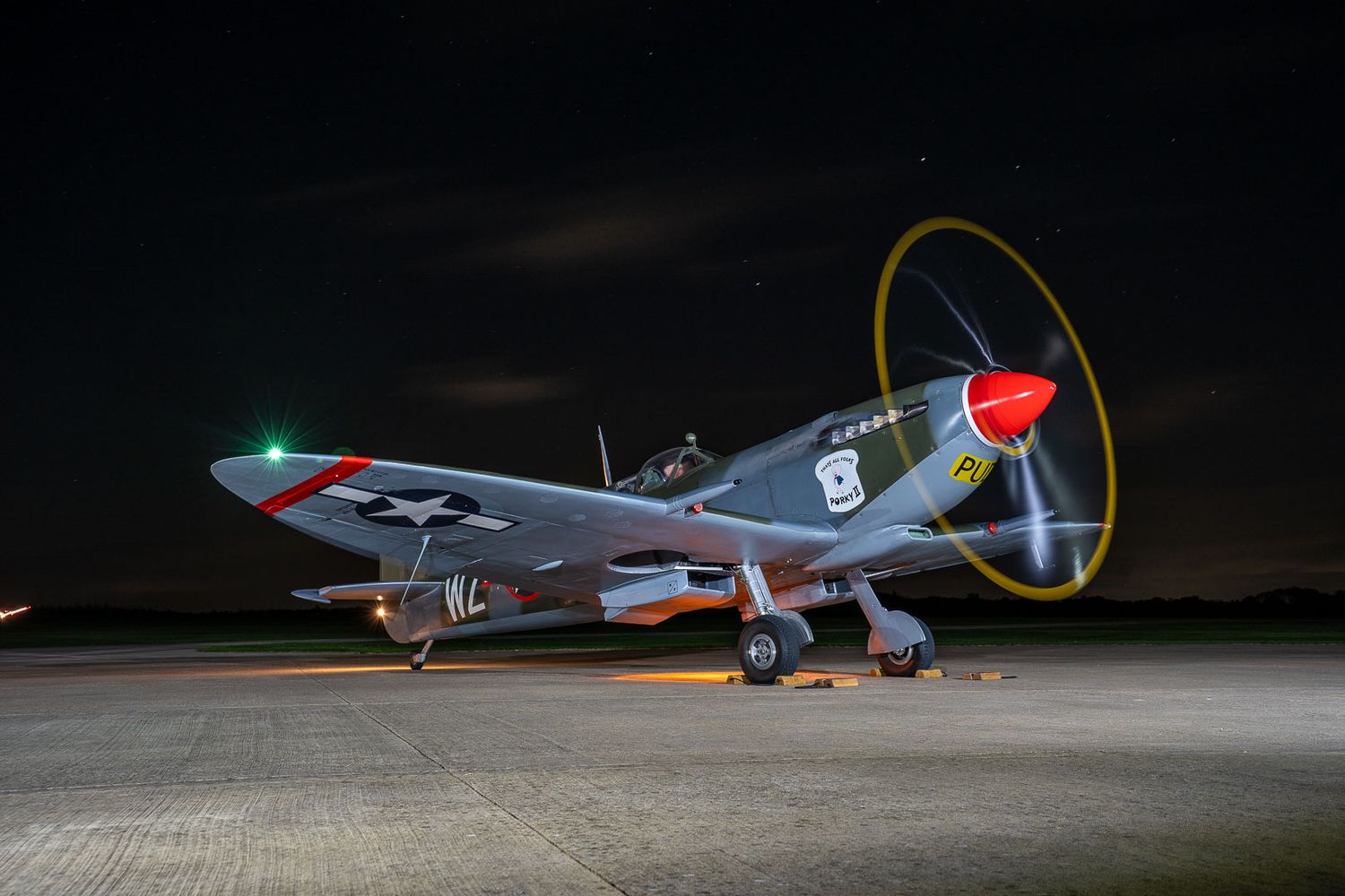 Vintage WWII Spitfire aircraft on a night airfield with spinning propeller captured in a long exposure photograph.