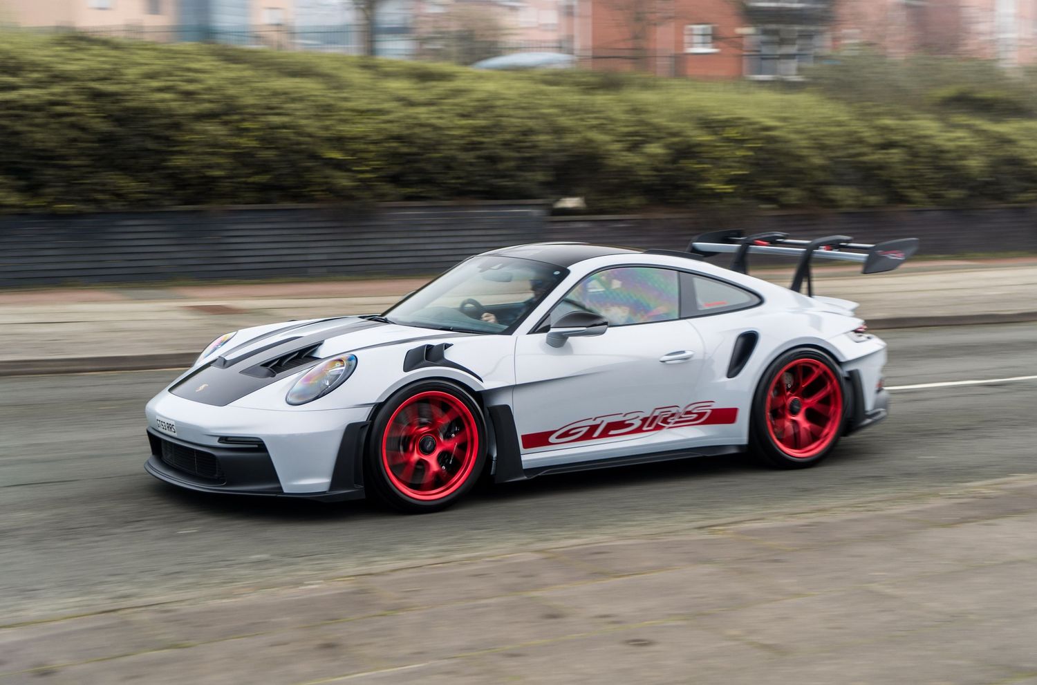 White Porsche 911 GT3 RS with red wheels and racing livery speeding on a city street.