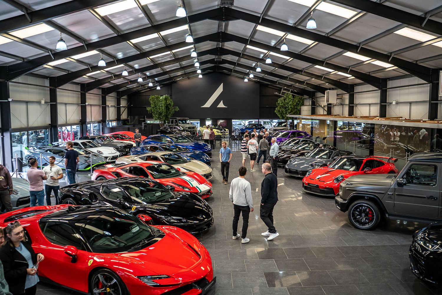 Luxury car showroom filled with red Ferraris and supercars with visitors browsing inside.
